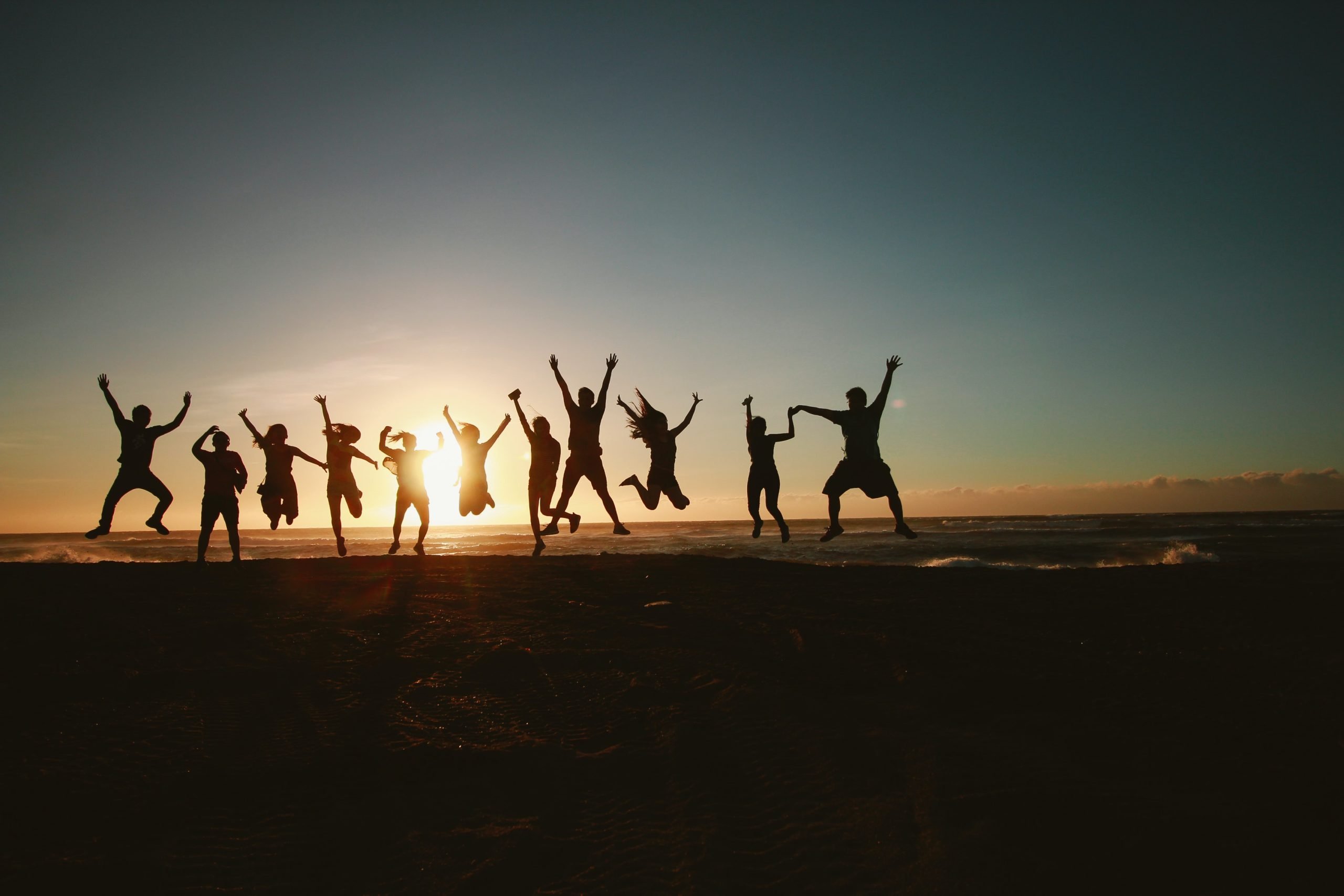 group of happy people jumping for joy as the sun sets